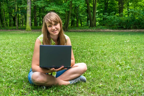 Parkta dizüstü bilgisayarı olan genç bir kadın.