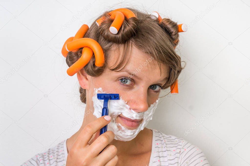 Young woman shaves her face with foam and razor