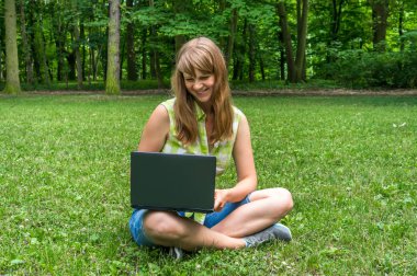Parkta dizüstü bilgisayarı olan genç bir kadın.