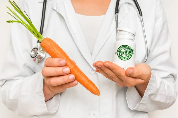 Female doctor compare pile of pills with fresh carrot — Stock Photo, Image