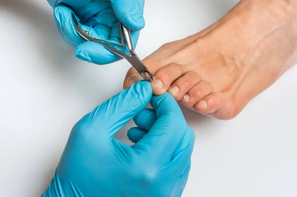 Pedicurist with nail clippers makes pedicure on female legs — Stock Photo, Image