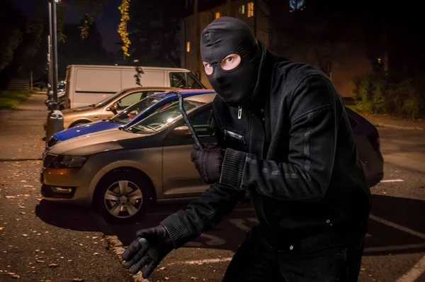 Maskerad tjuv i balaclava med kofot vill råna en bil — Stockfoto