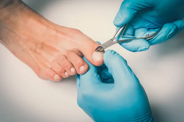 Педикюрст с ножницами делает педикюр на женских ногах — стоковое фото