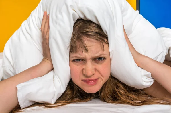 Mujer en cama cubriendo las orejas con almohada debido al ruido — Foto de Stock