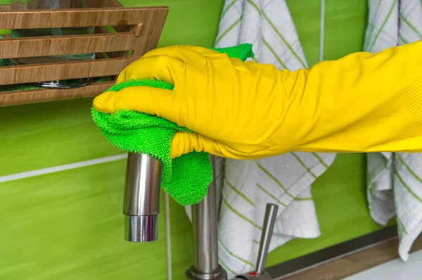 Hand in glove with green rag is wiping faucet in kitchen — Stock Photo, Image