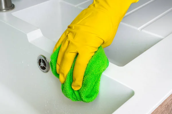 Hand in glove with green rag is wiping sink in kitchen — Stock Photo, Image