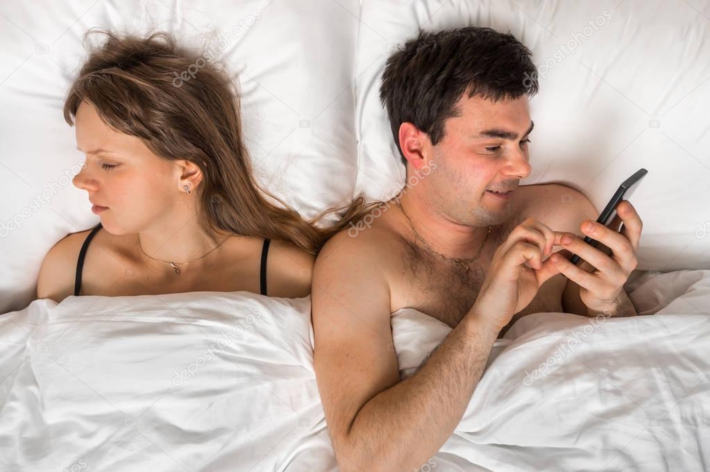 Young man using mobile phone, while his wife sleep at night