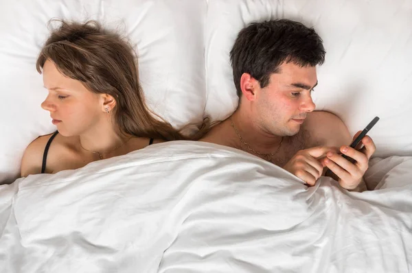 Young man using mobile phone, while his wife sleep at night — Stock Photo, Image