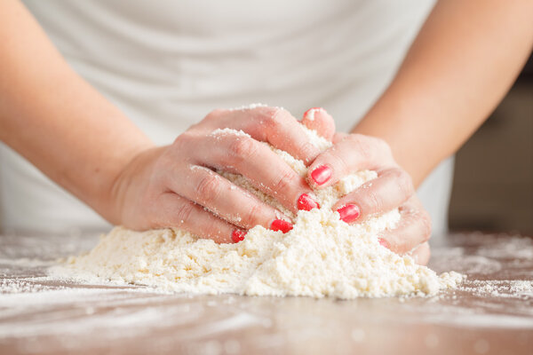 Hand of woman kneading dough for yeast cake on wooden table, pre