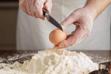Man breaks egg above white flour to make dough for ravioli or du clipart