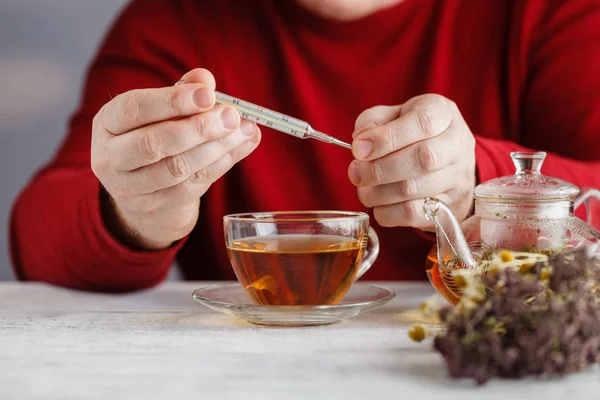 Erkälteter / kranker Mann mit Schal und Teetasse, der in Handtasche niest — Stockfoto