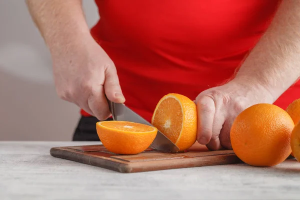 Рука режет апельсин на деревянной доске — стоковое фото