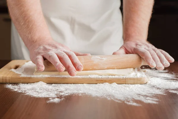 Padeiro rola a massa em uma mesa de cozinha de madeira polvilhada wi — Fotografia de Stock