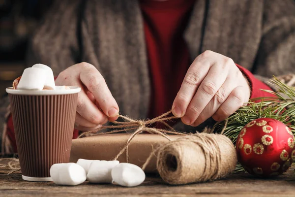 Male hand wrapped Christmas gift in the paper on dark wooden tab