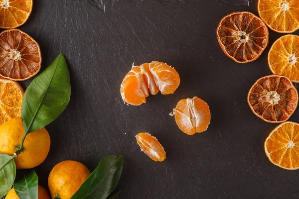 Tangerines with leaves and dry sliced orange over black slate su
