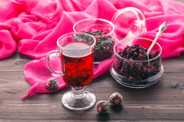 Чай Red Hot Hibiscus в стеклянной кружке на деревянном столе и сухой тэ — стоковое фото