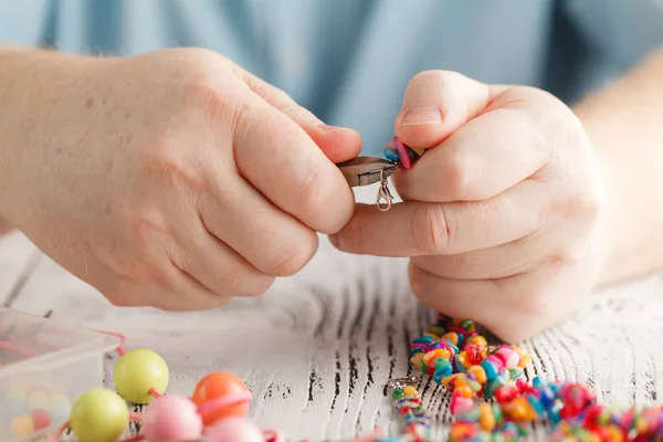 Persona haciendo pendientes de cuentas de colores y agujas — Foto de Stock