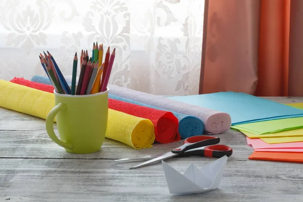 Set of origami boats and square sheets of colored paper on a woo