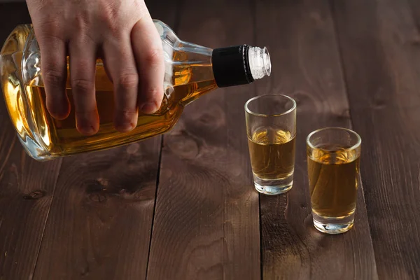 Derramando álcool em vidro de tiro na mesa de madeira — Fotografia de Stock