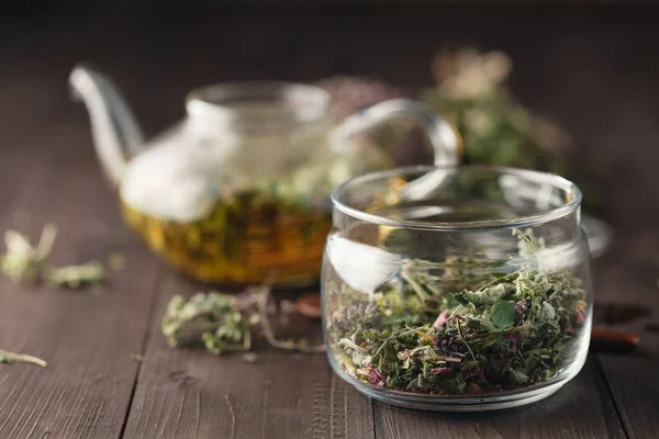 Сушеные травы на деревянном столе и чайник для чая — стоковое фото
