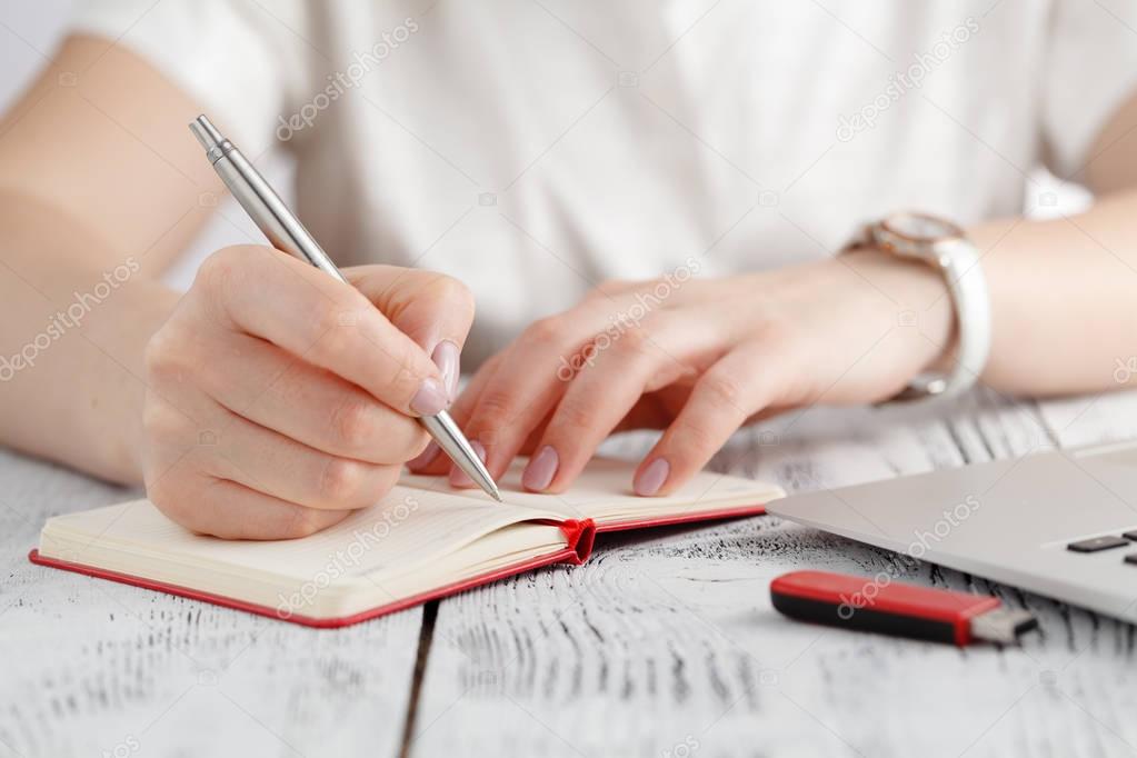 Female hands with manicure over pages of notebook hold a pen
