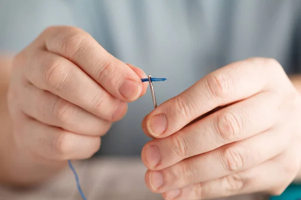 Thread into the needle. Close-up of man pulling thread into the