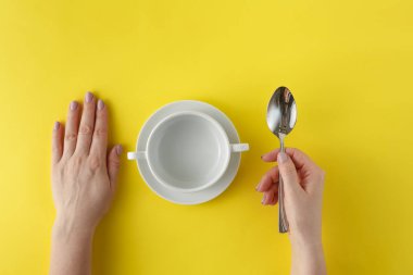 Elleriniz ve kaşık sarı arka plan boş beyaz tabakta. SOU