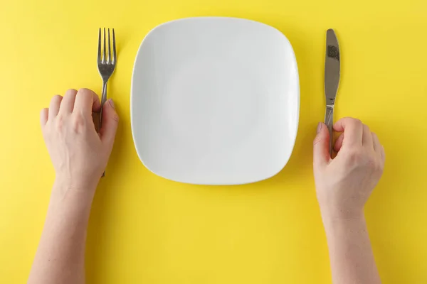 Mulher duas mãos segurar uma colher e garfo e prato branco em b amarelo — Fotografia de Stock
