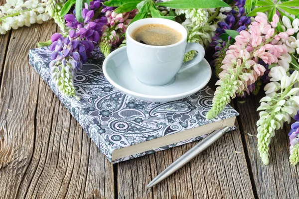 Megjegyzés: egy tollat és egy csésze kávét, csillagfürt virágok a fából készült asztal — Stock Fotó