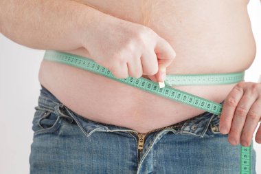 Adam göbeğini mezurayla ölçüyor.