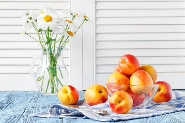 Fresh ripe peaches in bowl on blue wooden table and daisy in vas — Stock Photo, Image