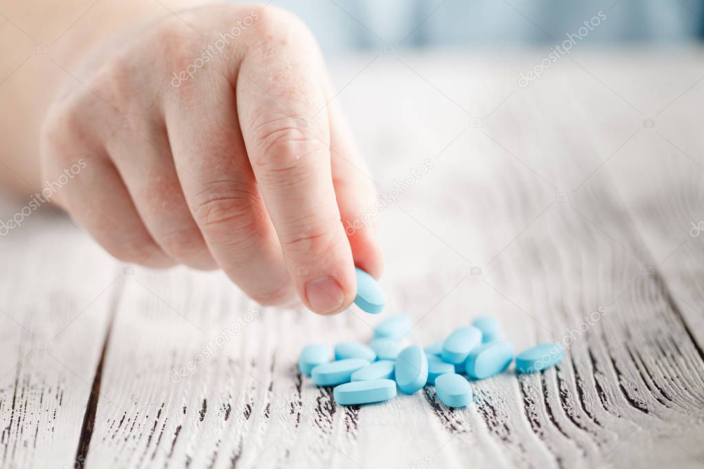 Male hand holding blue pill between fingers
