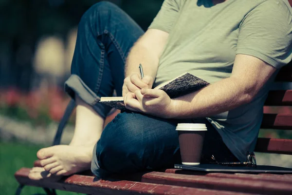 Homem escrevendo em seu caderno no parque — Fotografia de Stock