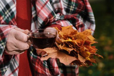 Adam akçaağaç yaprakları ile sonbahar Parkta yürümek çay fincan