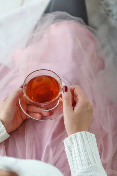 Vrouw in een grijze trui en warme sokken houden van een kopje thee terwijl zittend op een wit gebreid deken — Stockfoto