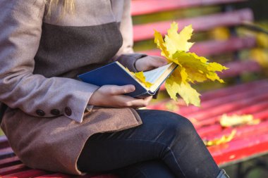 Kız parkta au akçaağaç yaprakları ve bir kitap tutan bir ceket