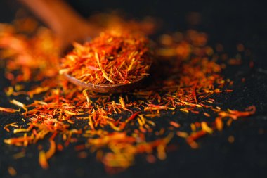 Siyah arka plan üzerine safran baharat kurumuş. Ham organik pistil toz safran masaya dağılmışlardır. Siyah arka plan üzerine bir tahta kaşık kırmızı safran baharat