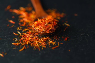 Siyah arka plan üzerine safran baharat kurumuş. Ham organik pistil toz safran masaya dağılmışlardır. Siyah arka plan üzerine bir tahta kaşık kırmızı safran baharat