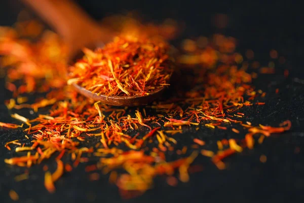 Siyah arka plan üzerine safran baharat kurumuş. Ham organik pistil toz safran masaya dağılmışlardır. Siyah arka plan üzerine bir tahta kaşık kırmızı safran baharat