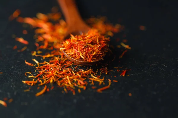 Dried saffron spice on black background. Raw Organic pistil powder saffron are scattered on the table. Red Saffron Spice in a wooden spoon on black background