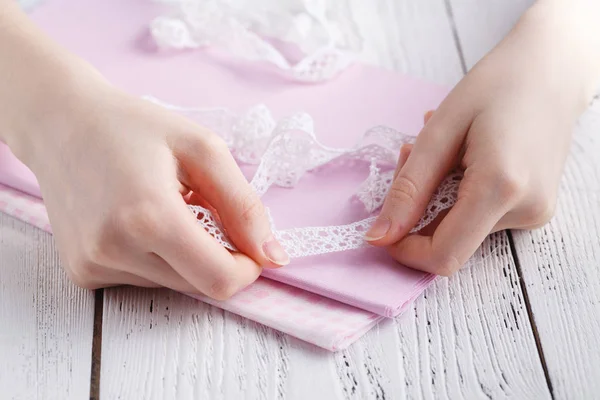 Haciendo decoraciones de mesa. Un tiro de mujer cosiendo un mantel de lino beige natural, toallas y servilletas con estampado de rosa y un ajuste de encaje de lino blanco de ganchillo, usando agujas — Foto de Stock