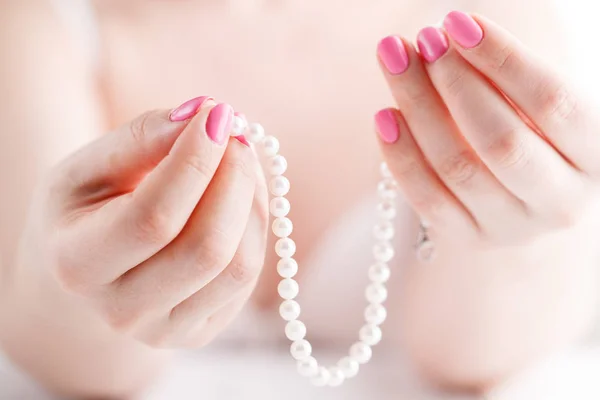 Perles blanches dans les mains des femmes, avec des ongles peints en rose — Photo