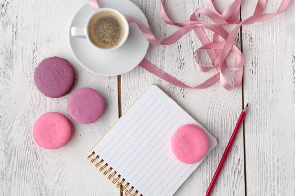 Coffee, cake macaron, clean notebook, eyeglasses and flower on pink table from above. Female working desk. Cozy breakfast. Flat lay style. — Stock Photo, Image