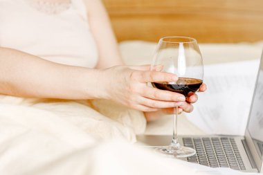 Yatakta uzanmış bilgisayar tableti seyreden ve bir bardak şarap içen kadın, sütyensiz, evde kal.