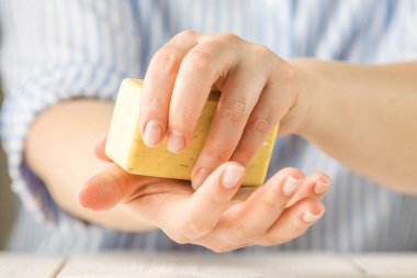 Kadın elleri sabun tutuyor. Ellerinde sabun köpüğü var. Sarı sabun. Kadın, virüsü korumak için sabunu elleriyle yıkıyor. COVID-19