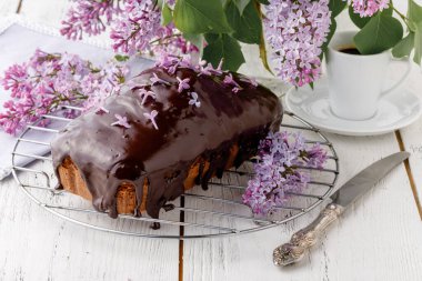 Brownie, ahşap arka planda çikolatayla sulandırılmış, bir buket leylakla.