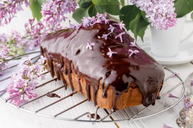 Brownie, ahşap arka planda çikolatayla sulandırılmış, bir buket leylakla.