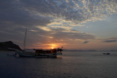 Arka plan kırmızı günbatımı üzerinde küçük bir gemi.