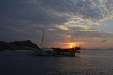 Arka plan kırmızı günbatımı üzerinde küçük bir gemi.