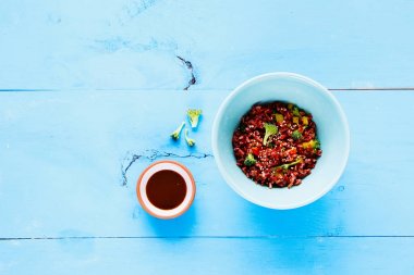 Lezzetli kırmızı pirinç ve brokoli kase. Vejetaryen, sağlıklı, diyet gıda kavramı. Hafif mavi ahşap masa üzerinde en iyi görünüm. Düz yatıyordu